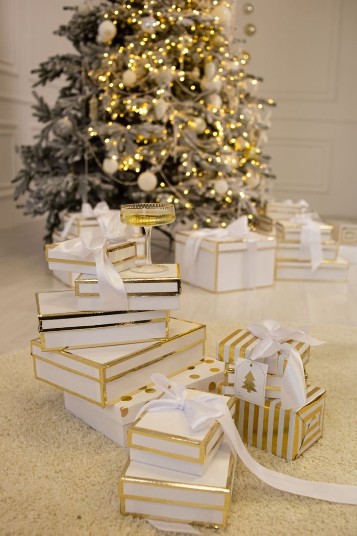 Festive white and gold Christmas gifts arranged beneath a decorated tree.