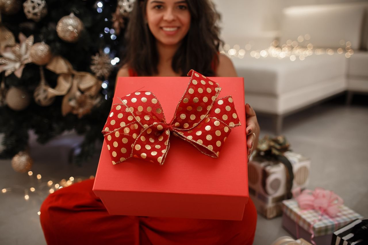 A cheerful young woman presenting a beautifully wrapped Christmas gift indoors.