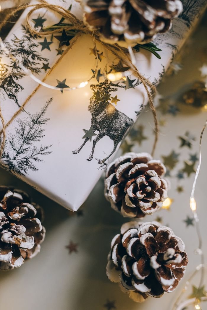 A wrapped Christmas gift with pine cones and fairy lights, creating a cozy holiday atmosphere.
