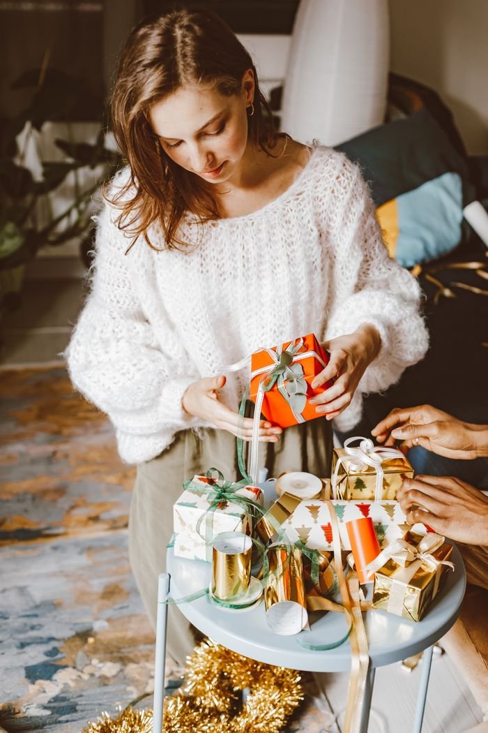 about-us A woman wraps Christmas gifts with decorative ribbons in a cozy indoor setting.